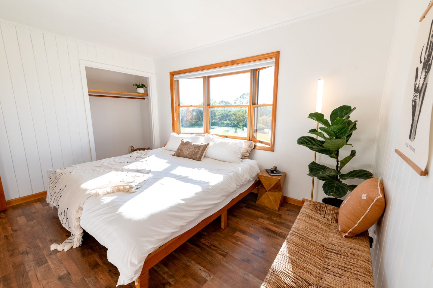 Dormitorio con cama de madera, piso de madera y ventana amplia